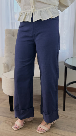 Person wearing navy pants and a white top in a room with a chair and table.