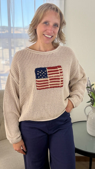 Woman wearing a beige sweater with an American flag design, standing in a living room.