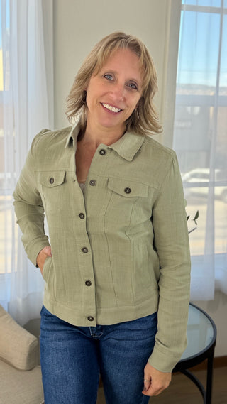 Woman wearing a green jacket and blue jeans indoors.