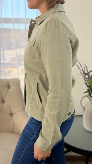 Person wearing a light green jacket and blue jeans in an indoor setting.
