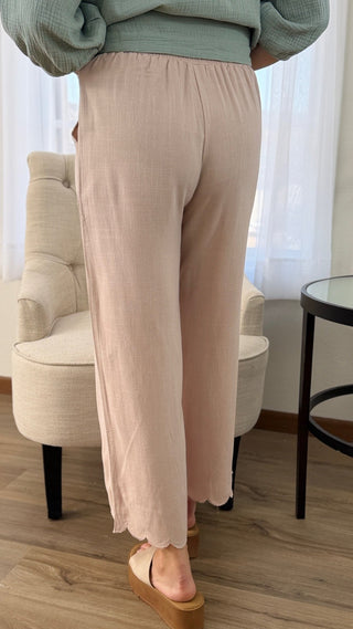 Person wearing light pink pants and a green top in a room with a chair and table.