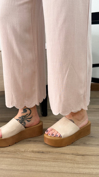 Person wearing beige sandals with brown soles on a wooden floor.
