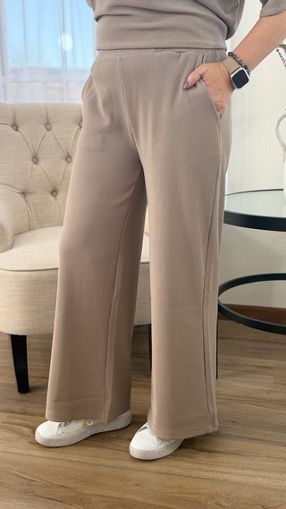 Person wearing beige wide-leg pants and white sneakers in a room with a tufted chair.