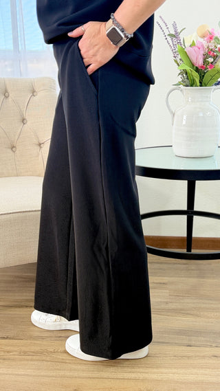 Person wearing navy blue wide-leg pants standing in a room with a couch and table in the background.
