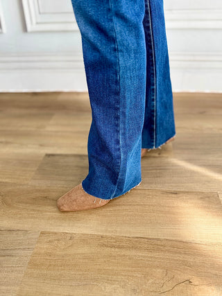 Person wearing blue jeans and brown shoes on a wooden floor.
