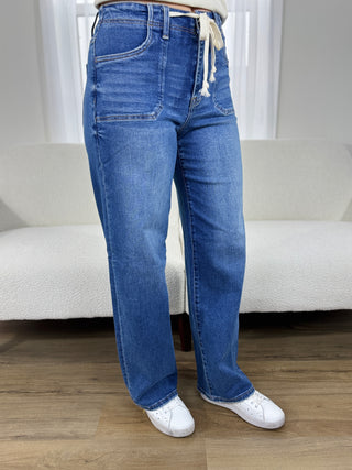 Person wearing blue jeans and white sneakers standing in a room with a white couch and light-colored walls.