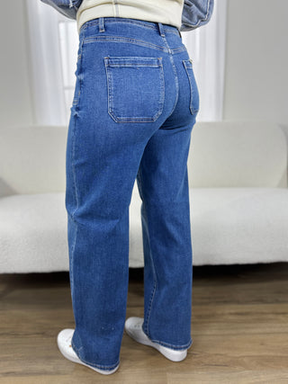 Person wearing blue jeans standing in a room with a white couch and wooden floor.