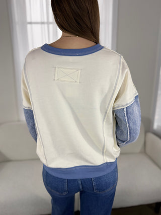 Person wearing a white and blue sweater with a visible brand logo, standing in a room with a neutral background.