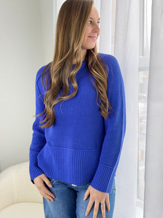 Woman wearing a blue sweater in a bright room with white curtains.