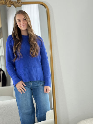 Woman wearing a blue sweater and jeans standing in front of a mirror.