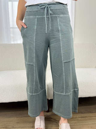 Person wearing green wide-leg pants with a white couch in the background