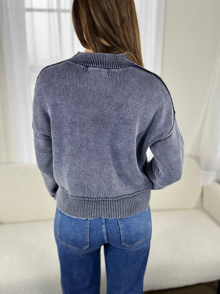 Person wearing a blue sweater and jeans in a neutral setting