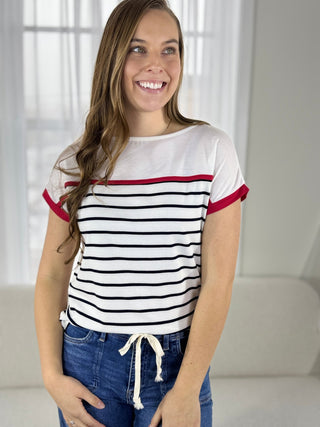Woman wearing a striped shirt with red and black trim in a bright room.