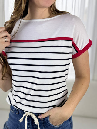 Person wearing a white t-shirt with black and red stripes, standing against a plain background.