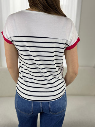 Person wearing a white t-shirt with black and red stripes and blue jeans indoors.