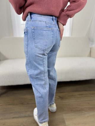 Person wearing light blue jeans and a pink sweater in a room with a white couch.