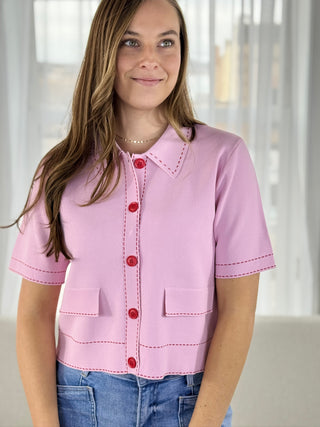 Woman wearing a pink blouse with red buttons and blue jeans indoors.
