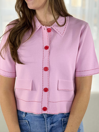 Pink shirt with red buttons worn by a person on a white background