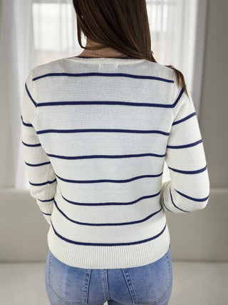 Person wearing a white sweater with blue stripes and blue jeans indoors.