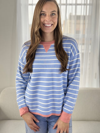 Woman wearing a blue and white striped sweater with pink accents in a bright room.