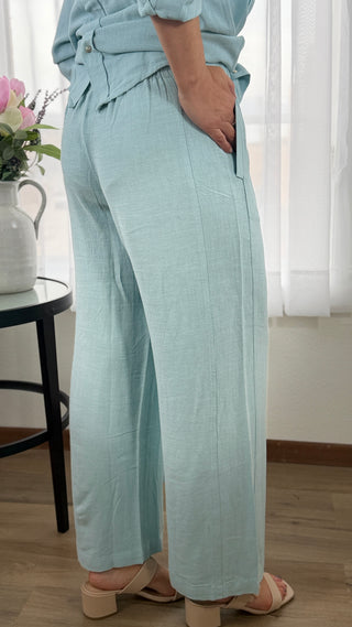 Person wearing light blue pants standing in a room with a table and flowers.