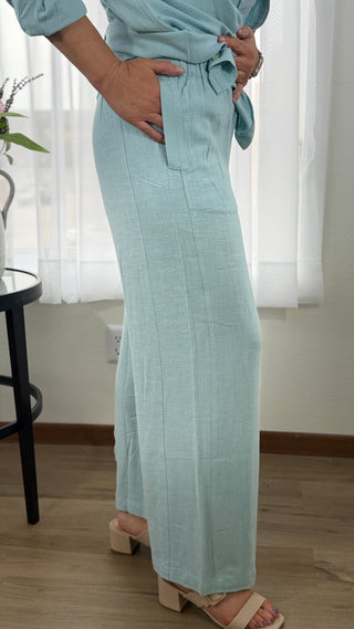 Person wearing light blue pants and a matching top in a room with white curtains.