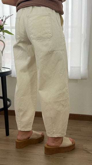 Person wearing beige pants in a room with white curtains and a wooden floor.