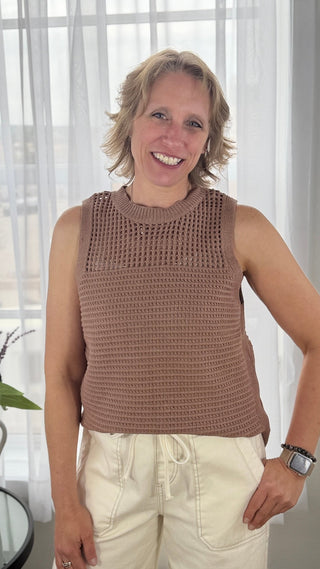Woman wearing a brown sleeveless crochet top in a bright room.