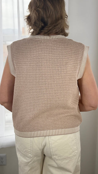 Person wearing a beige knitted vest indoors.