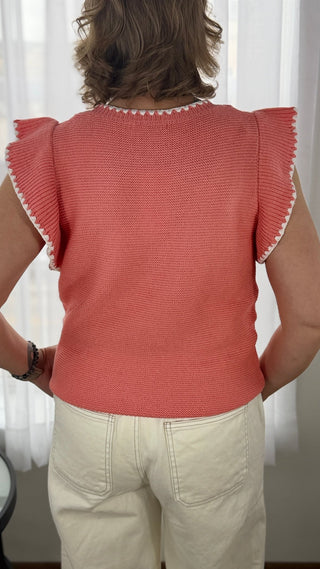 Person wearing a red top with ruffled sleeves and beige pants against a white curtain background