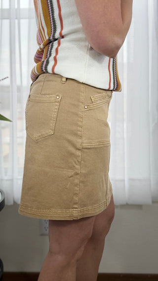 Person wearing a beige skirt with a striped shirt in a room with white curtains.