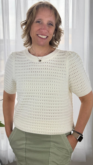 Woman wearing a white crochet top with a neutral background