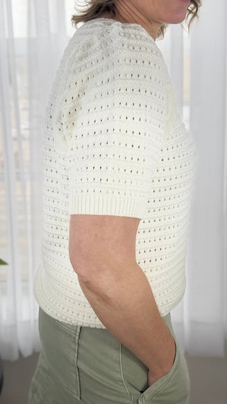 Person wearing a white crochet top with a blurred background