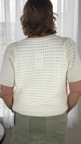 Person wearing a cream-colored crochet top with a blurred background