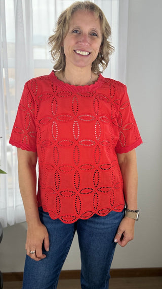 Woman wearing a red lace top and blue jeans indoors.