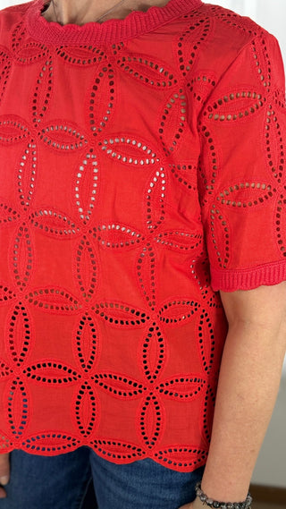 Red top with cut-out patterns worn by a person, against a neutral background