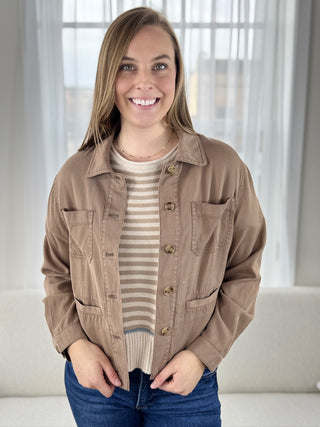 Woman wearing a brown jacket over a striped shirt with a neutral background