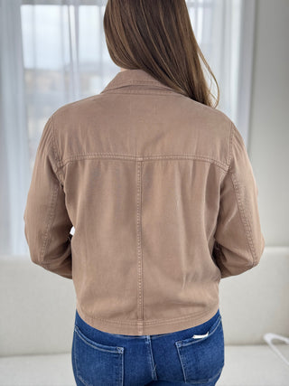 Person wearing a brown jacket and blue jeans in a neutral setting