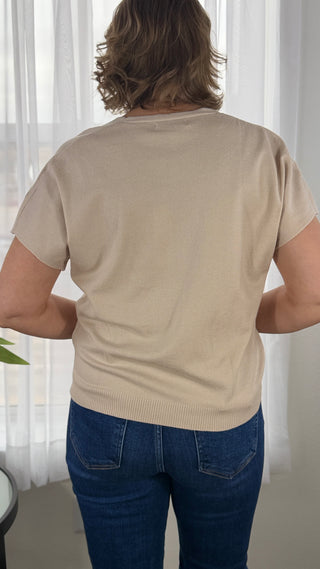 Person wearing a beige sweater and blue jeans standing in front of white curtains.