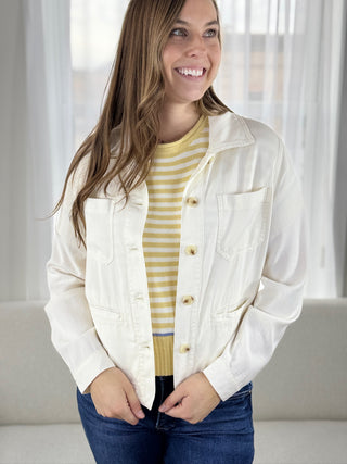 Woman wearing a white jacket over a yellow striped shirt in a bright room.