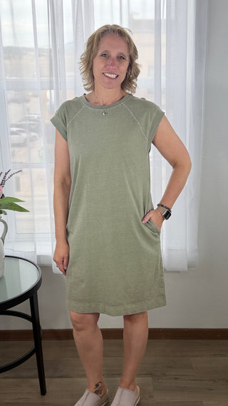 Woman wearing a green dress standing in a room with white curtains.