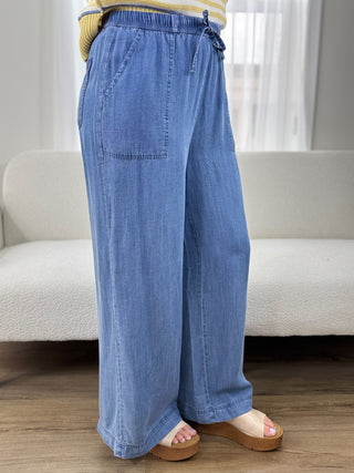 Person wearing blue wide-leg jeans standing in a room with a neutral color scheme.