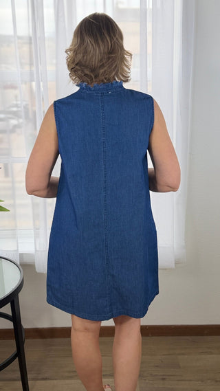 Woman wearing a blue denim dress in a room with white curtains.