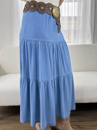 Blue tiered dress with a decorative belt worn by a person, sitting on a couch.