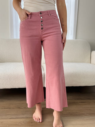 Person wearing pink pants with buttons standing in a room with a couch and curtains.