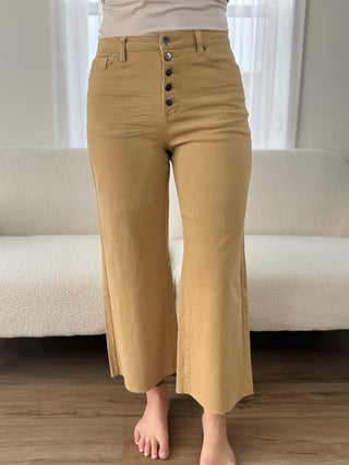 Person wearing beige pants with button details in a minimal indoor setting