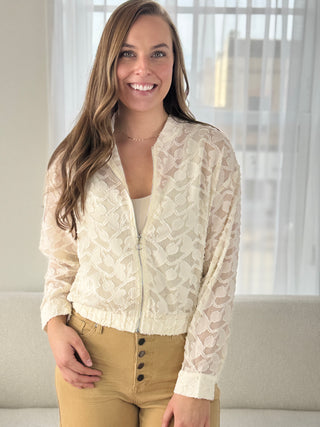 Woman wearing a beige lace cardigan over a beige top and pants indoors.