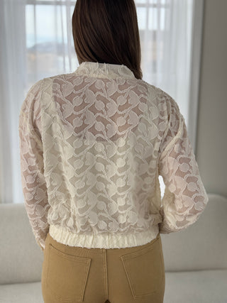 Person wearing a beige lace blouse with a blurred background
