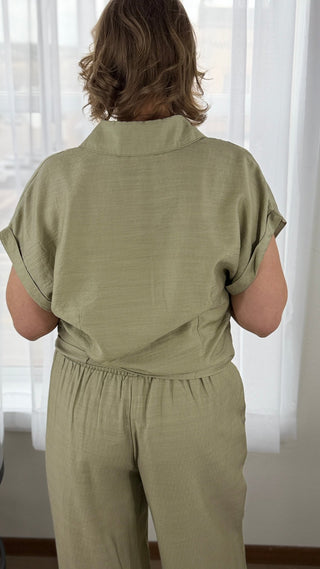 Person wearing a green jumpsuit standing in front of white curtains