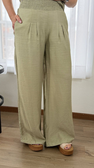 Person wearing olive green wide-leg pants in a room with white curtains.